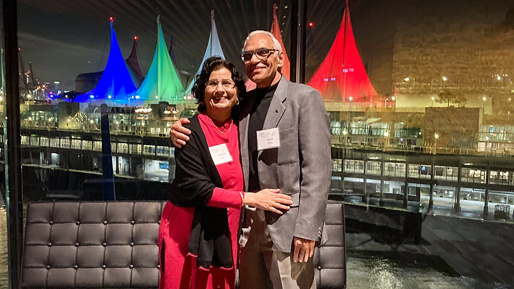 A man and woman pose with their arms around each other. In the background