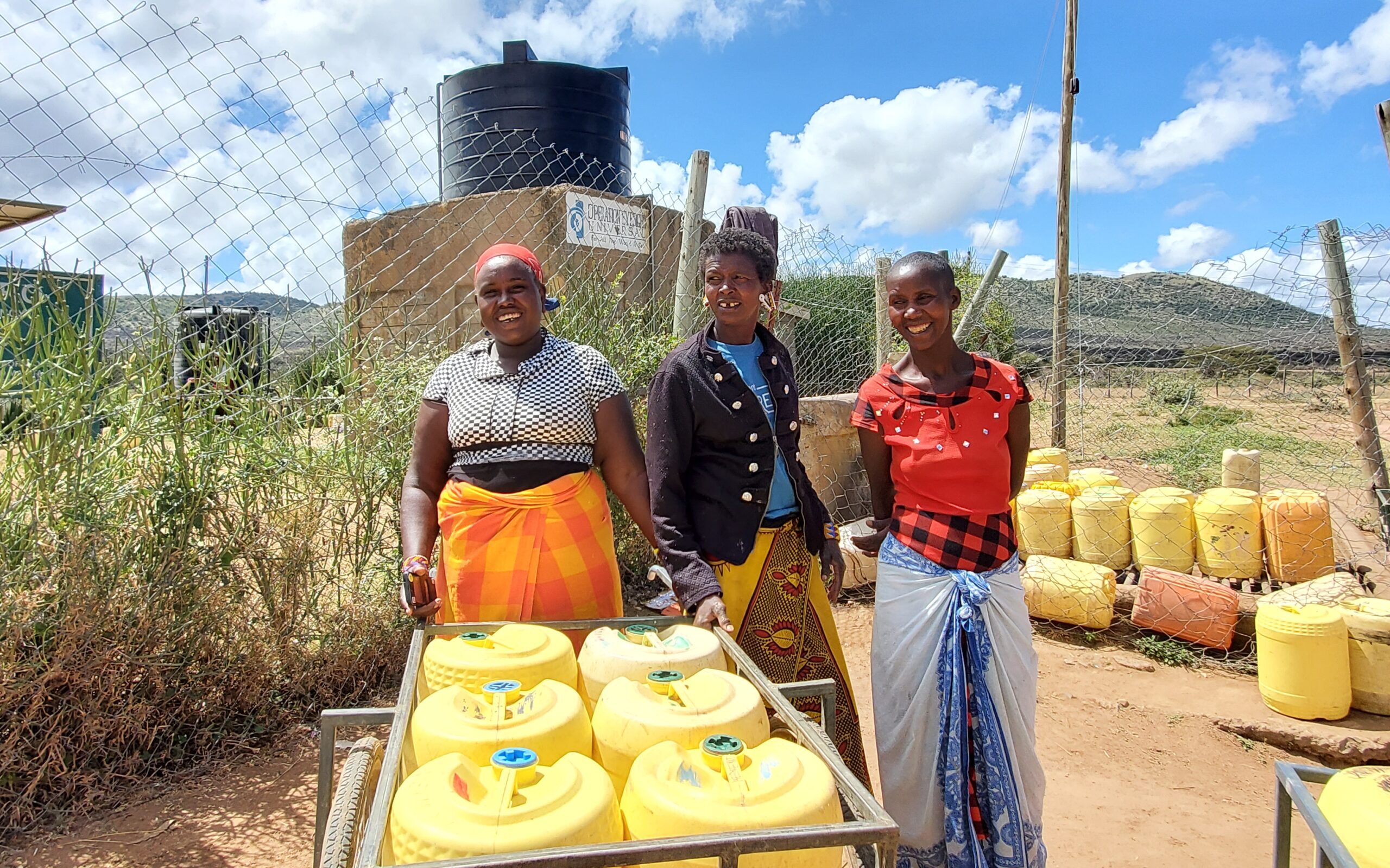 Three women smile as they collect water from a water tank|Three students standby a borehole as one of them drinks water from it|A water tank|A student washes her face with water from a pipe. Her teacher and classmates stand closely.