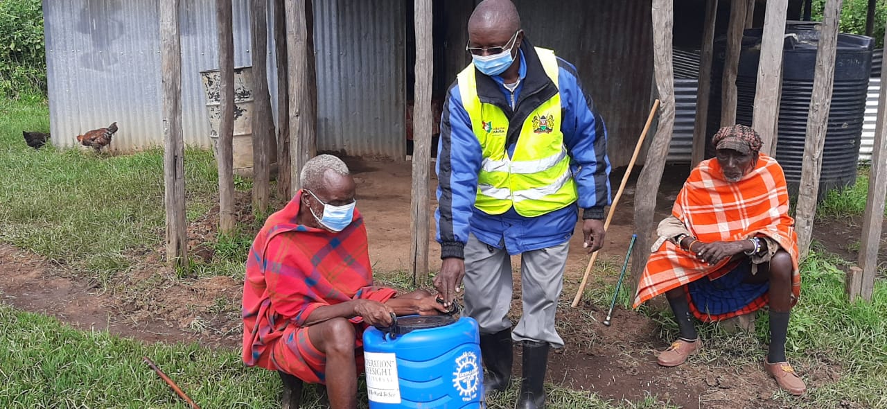 Blind man receives hand washing vessel from public health officer in Narok|A woman wearing adjustable trial lens frame