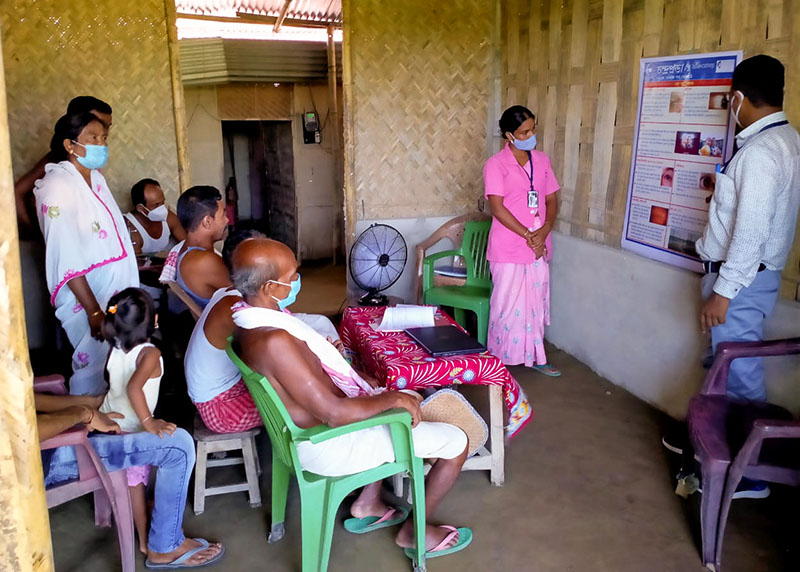 A community health worker educates a group of people on eye health using a poster affixed to a wall|A group of women gather around educational materials in a room with blue walls.|An instructor speaks to a group of students seated at desks in a classroom.|A healthcare worker uses a small