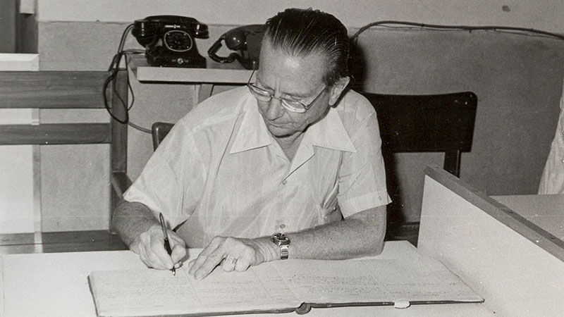 A black and white historical photo shows Art Jenkyns busily working at his office desk.|A black and white photo from a hospital room with healthcare staff watching over patients