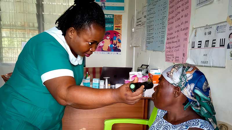 Woman examines the eye of a female senior with a small light.|Woman standing at the front of a classroom holds a diagram with various eye conditions as students look on.|Woman stands at the front of a classroom holding a desplay with various eye conditions