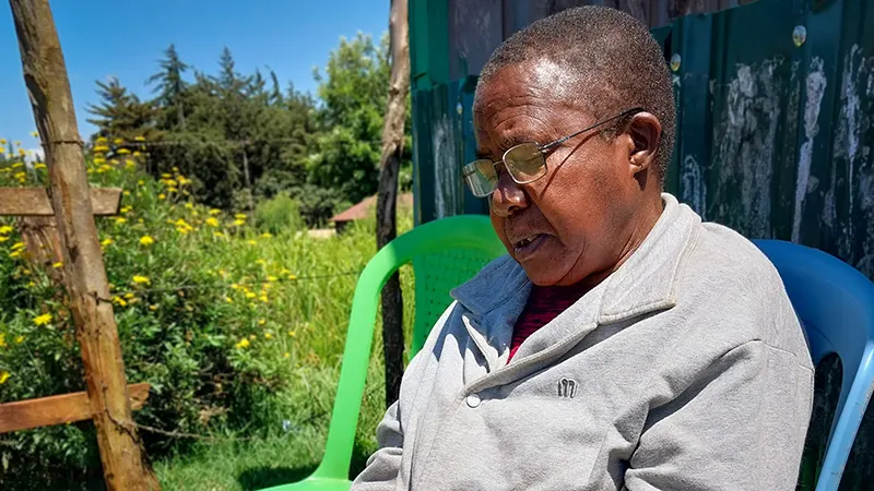 A woman wearing glasses sits outdoors in a blue chair.|Portrait of grandmother reading a book with her new eye-glasses.
