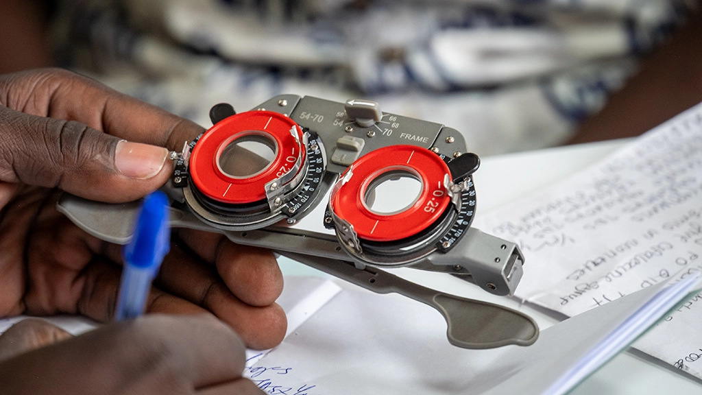 Optical frames used for refraction are held in a man's left hand while the right hand jots down notes.||||