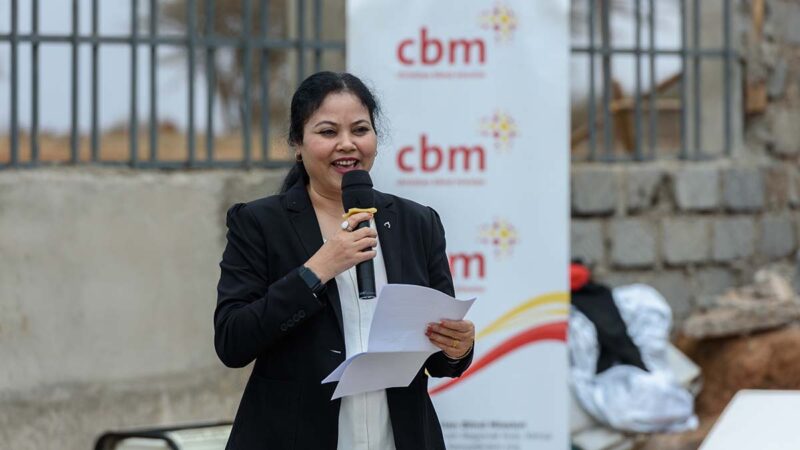 A woman speaking into a microphone.||A group of people cut a ribbon and the entrance of a building.||A group of people cut a ribbon and the entrance of a building.|Four women pose together for a photo.