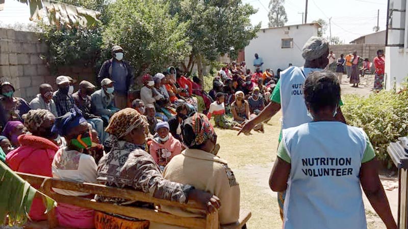A community gathered together to hear from nutrition volunteers|A group of people seated in a circle have a discussion during an eye care training|Two woman