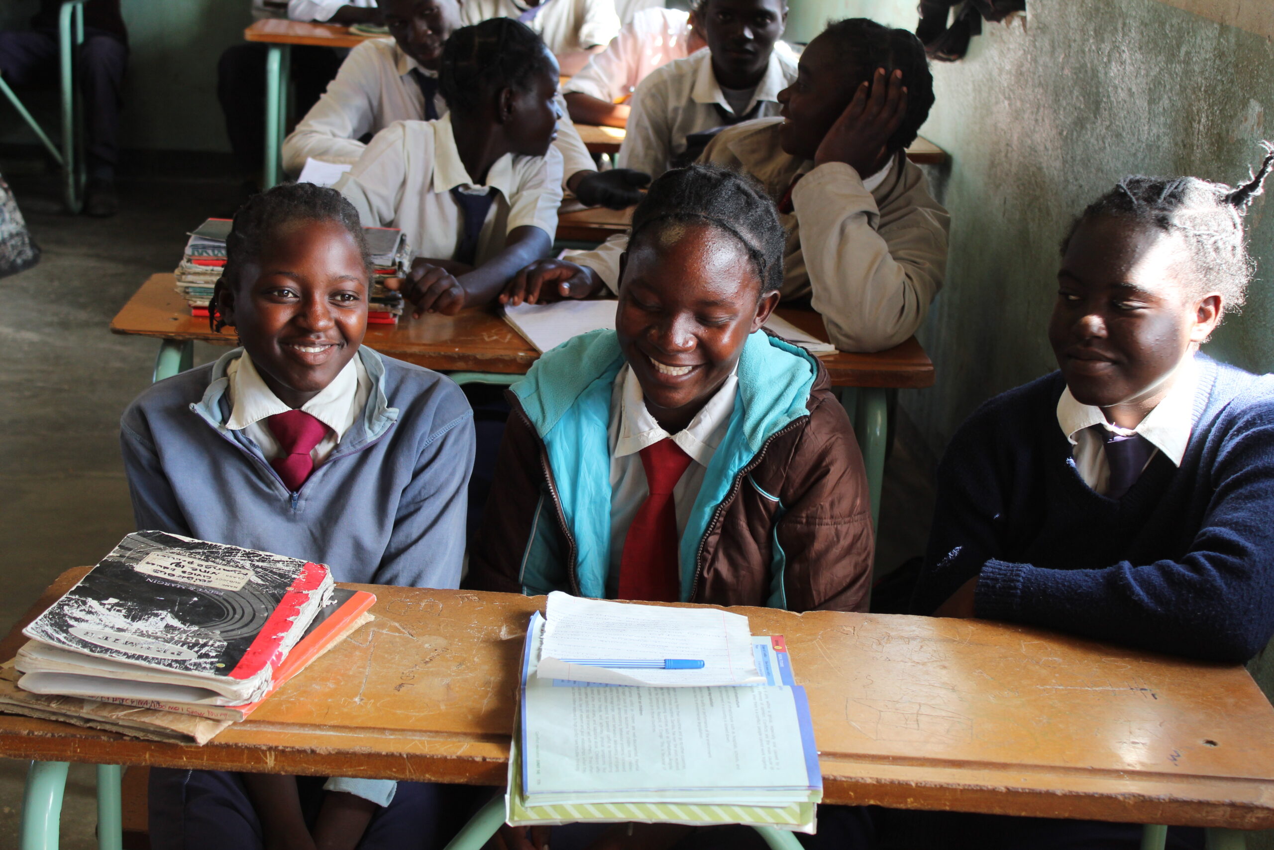 Group of young girls smiling at school in Zambia.|Young boy writing in school in Kenya