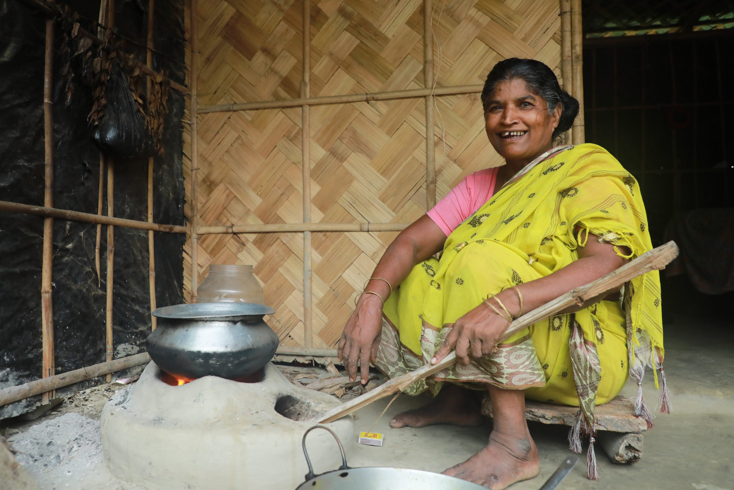 Savitri in her kitchen sitting by a stove made of mud.|Sabitri stands with her family members and a community health worker in front of her home.