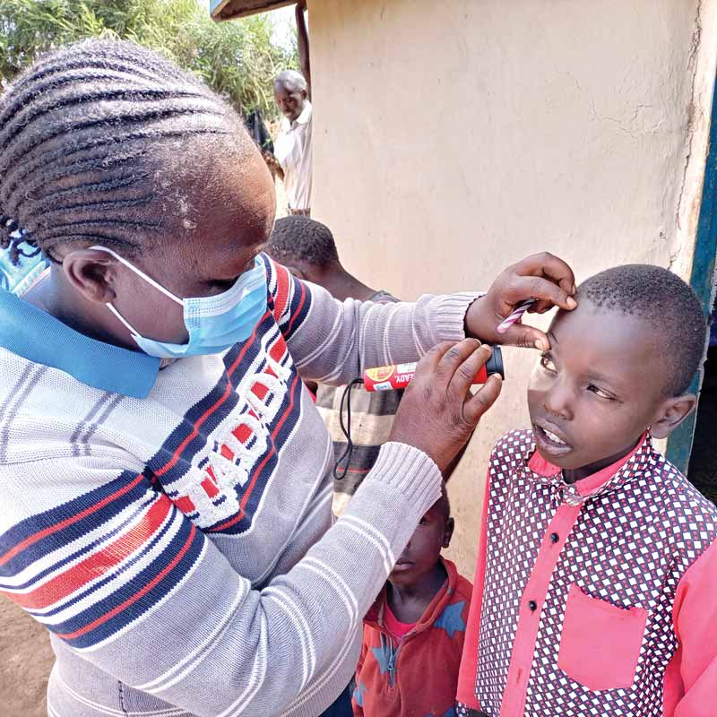 A community health worker checks the right eye of a young boy using a flashlight|A community health worker holds a book for a senior woman