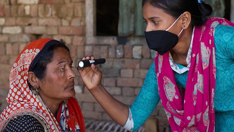 A young woman looking into the eyes of a senior woman using a flash light.|A grandmother with her grandson