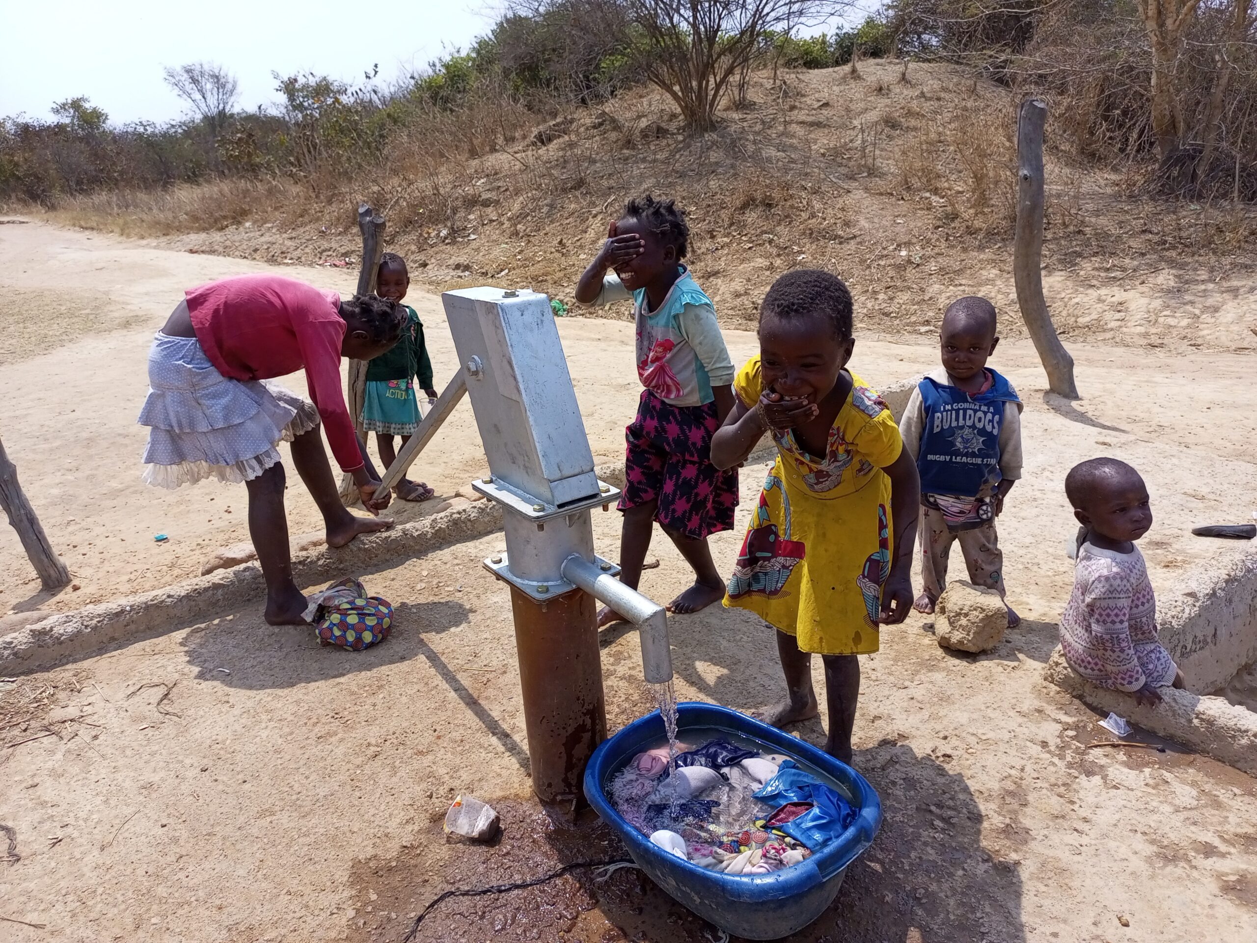 Children joyfully splash water on the faces at the newly-rehabilitated borehole in the village of Lukanda B